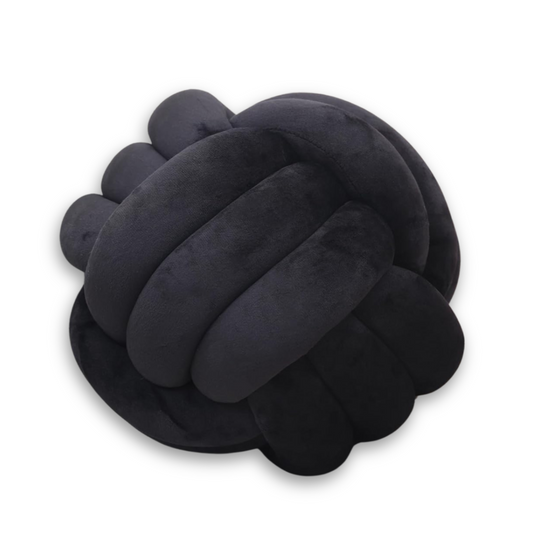 Black round velvet knot throw pillow in a sculptural twisted design on a dorm bed.