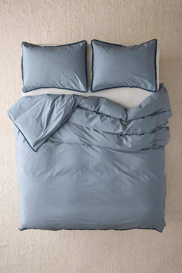 Overhead view of a blue duvet cover & shams with fringe detailing and matching pillows for dorm bed.