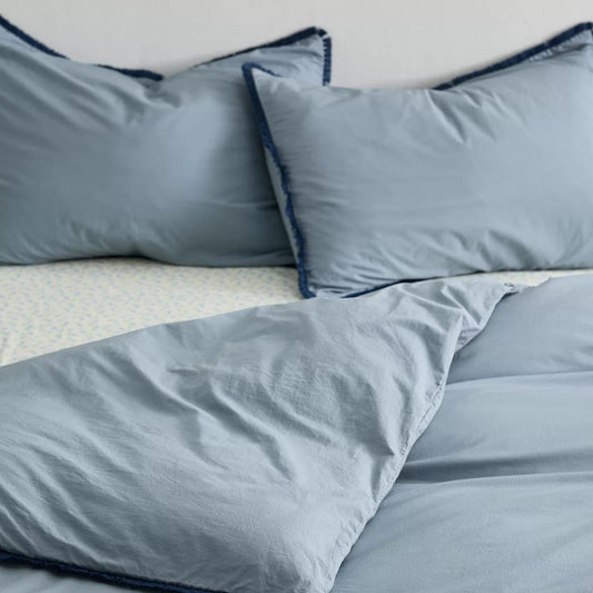 Overhead view of a blue duvet cover with fringe detailing and matching pillows on a dorm bed.