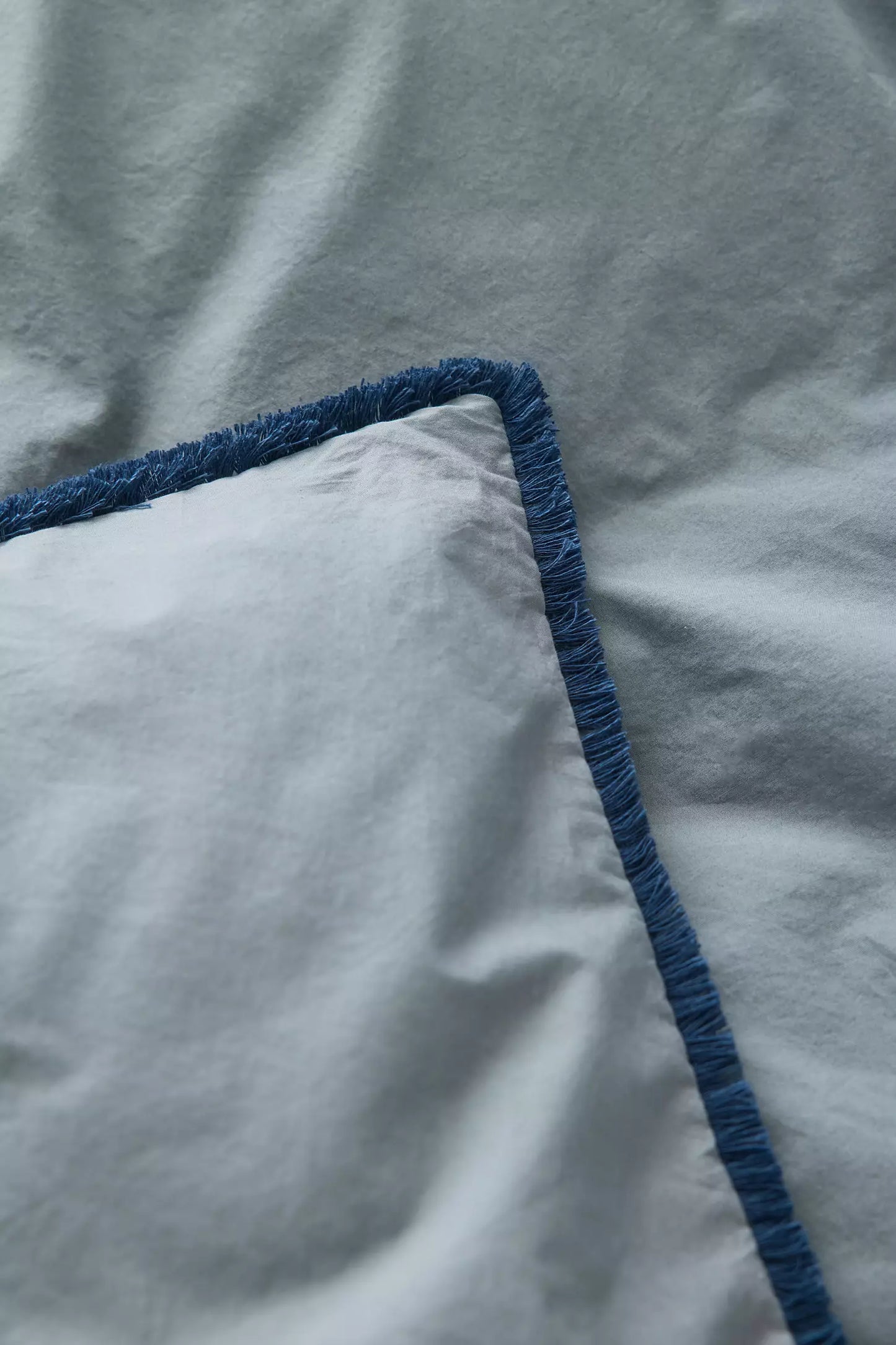 Overhead view of a blue duvet cover with fringe detailing and matching pillows on a dorm bed.