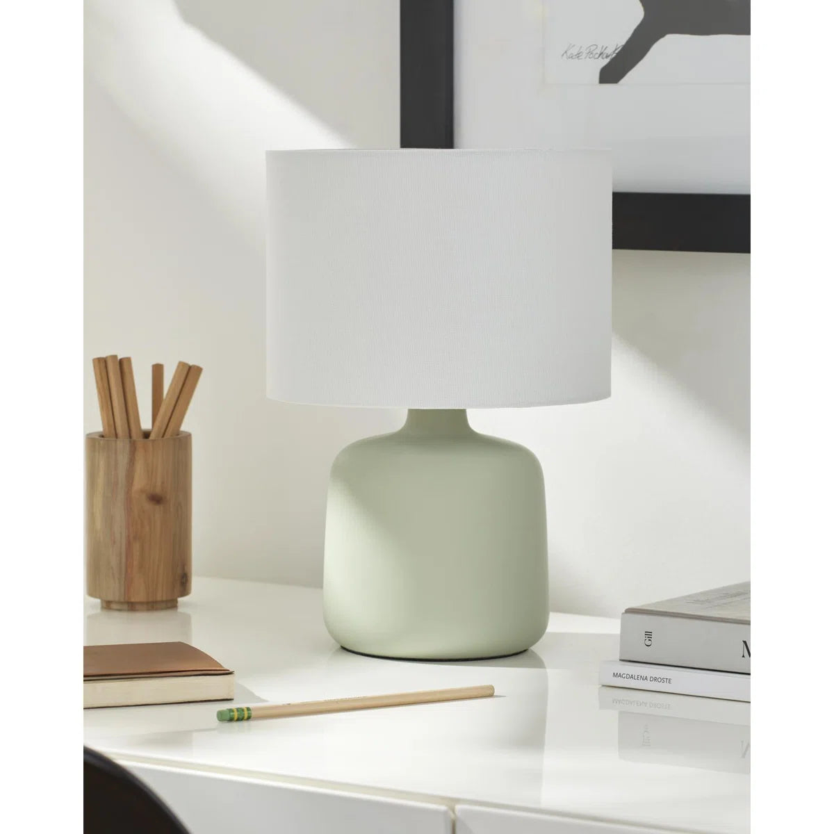 Green table lamp with a white shade on a desk with books and stationery for dorm