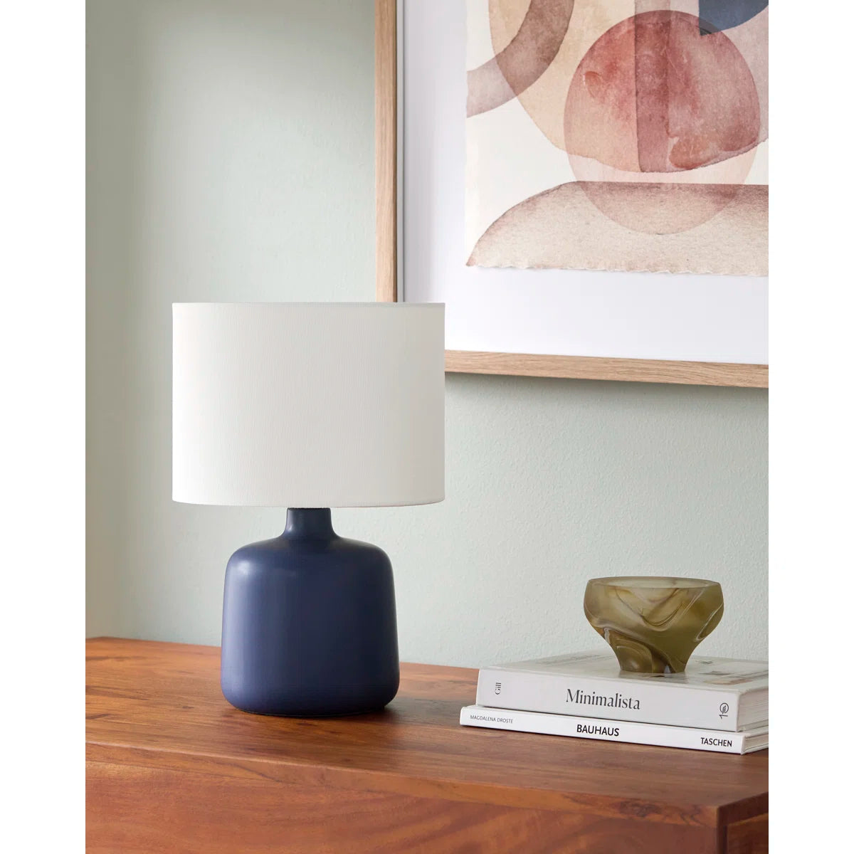 Navy blue table lamp with white shade on a wooden surface, with books afor dorm