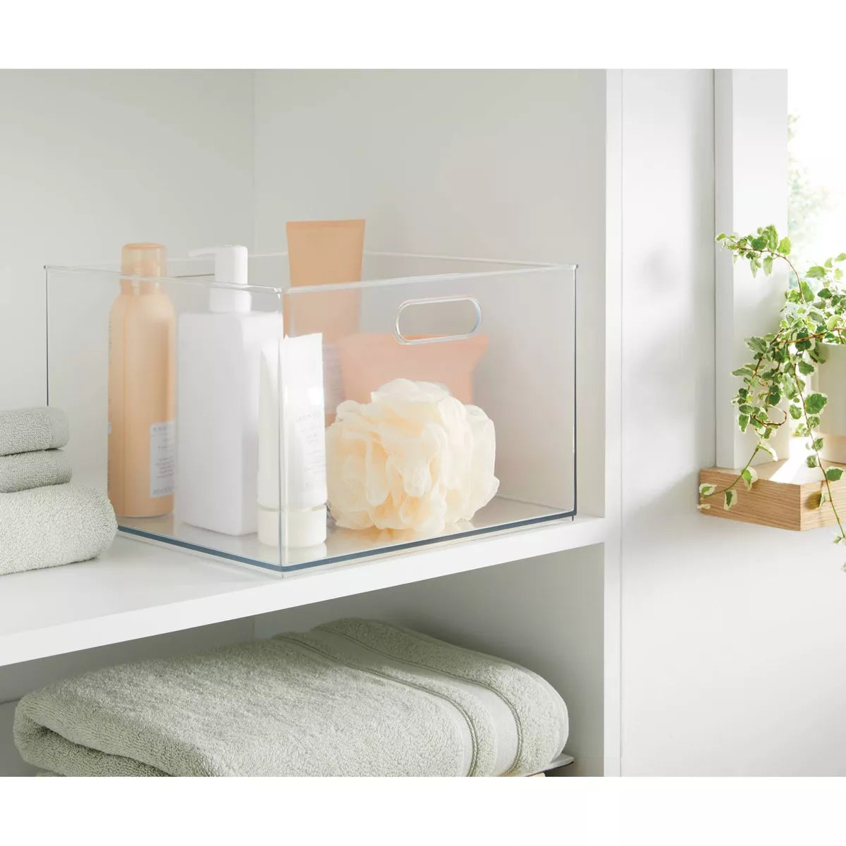 Clear storage basket with bath products on a white shelf in a bathroom setting.