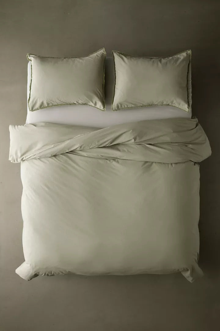 Overhead view of a sage duvet cover & shams with fringe detailing and matching pillows for dorm bed.