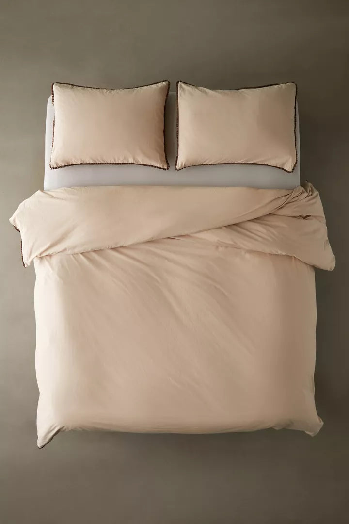 Overhead view of a tan duvet cover & shams with fringe detailing and matching pillows for dorm bed.