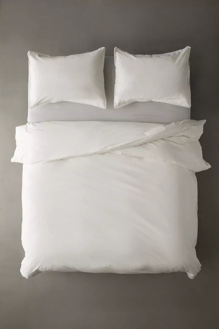 Overhead view of a white duvet cover & shams with fringe detailing and matching pillows for dorm bed.