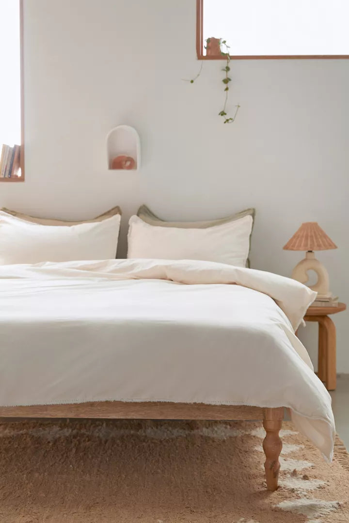 Overhead view of a white duvet cover & shams with fringe detailing and matching pillows for dorm bed.